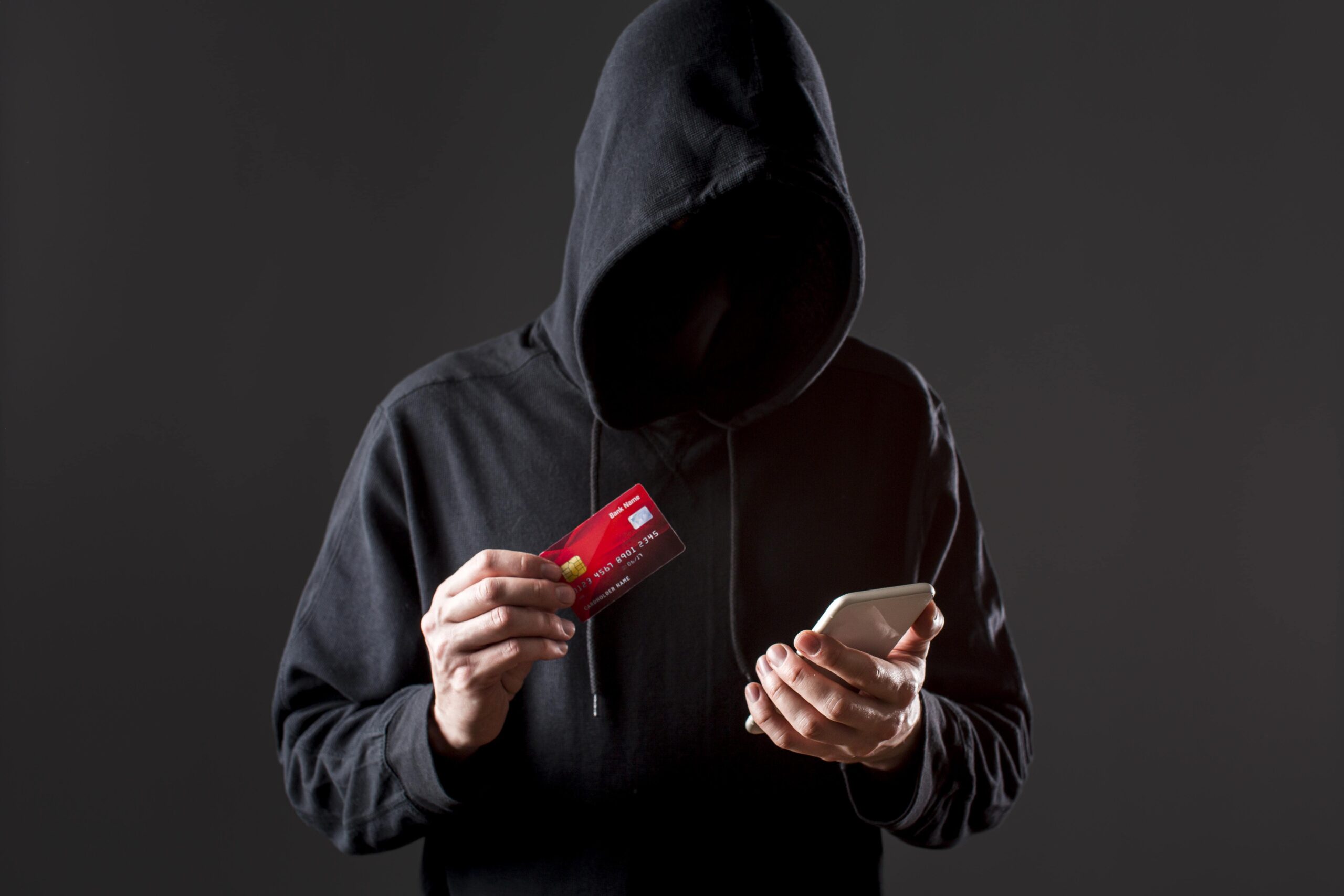 Hooded figure holding a credit card and smartphone, representing cybercrime and identity theft—areas Cyprus lawyers can help address legally.