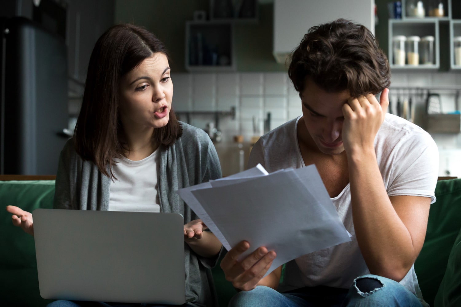 Couple sitting on a couch looking stressed, with the woman holding a laptop and the man reviewing documents, discussing legal or financial issues related to Cyprus lawyers.