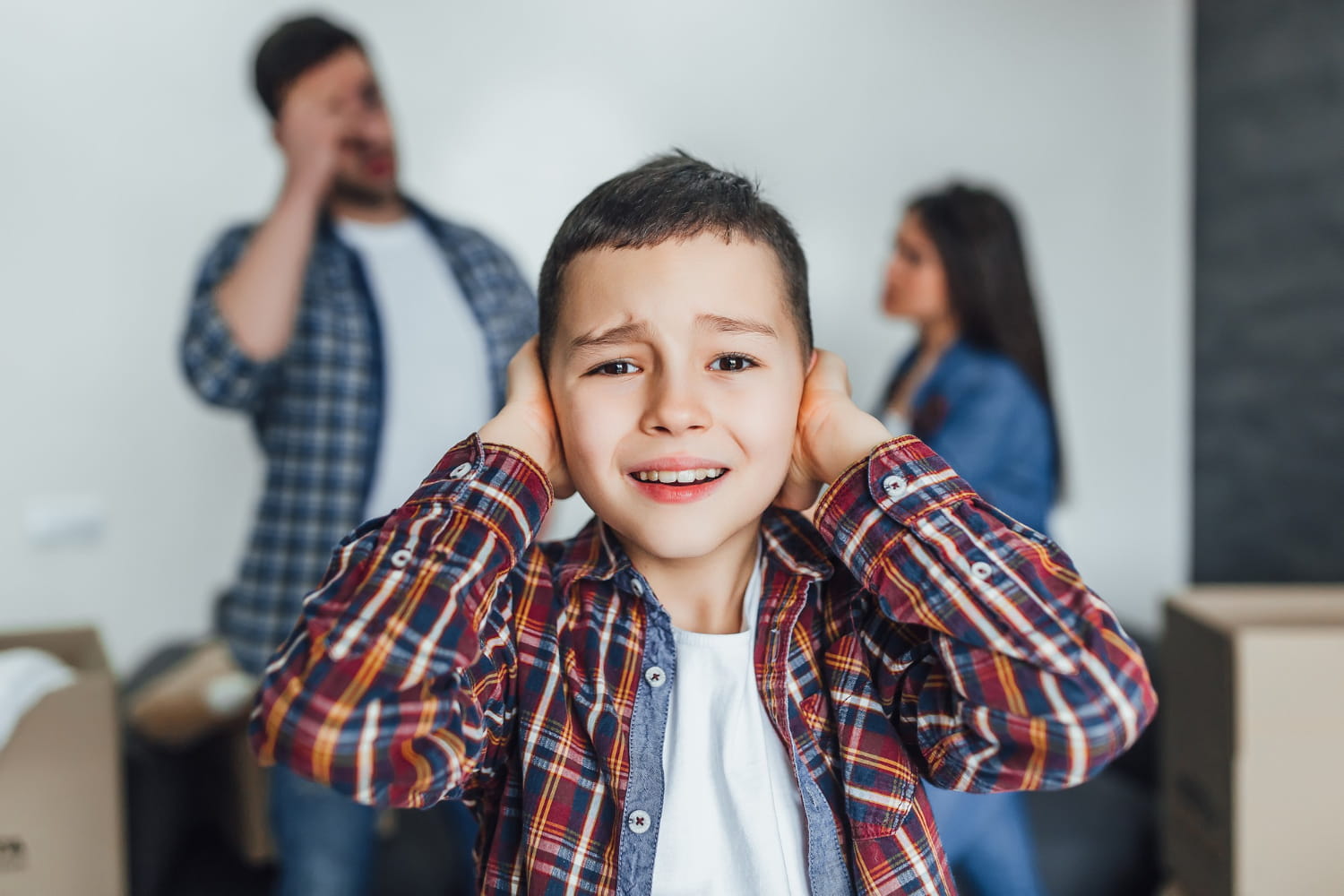 Distressed young boy covering his ears while parents argue in the background, illustrating a child custody dispute and family law case in Cyprus.